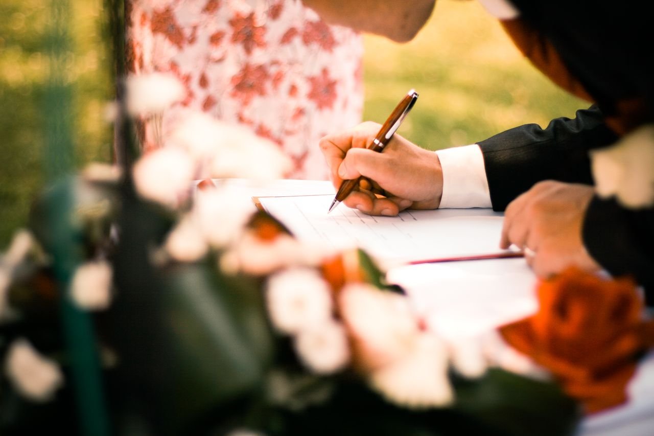 The Art of Drawing Readers In: Your attractive post title goes here A close-up of hands signing a marriage contract during an outdoor wedding ceremony